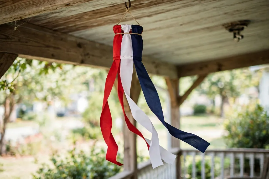 A ribbon windsock with red, white, and navy ribbons hanging from a porch ceiling.