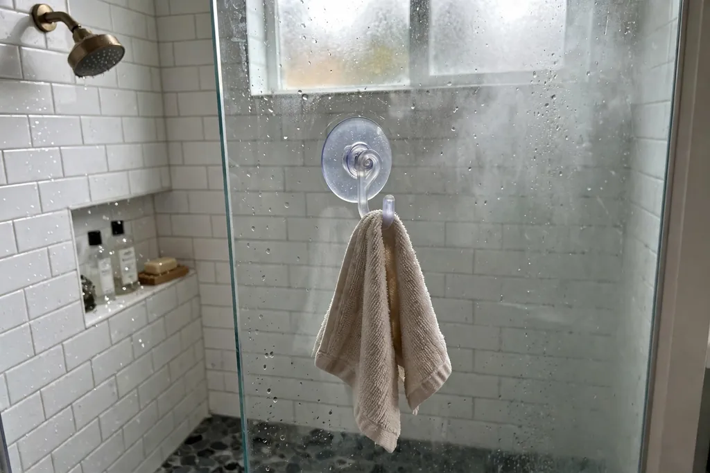 Suction cup hook on shower glass holding a small towel inside a shower.