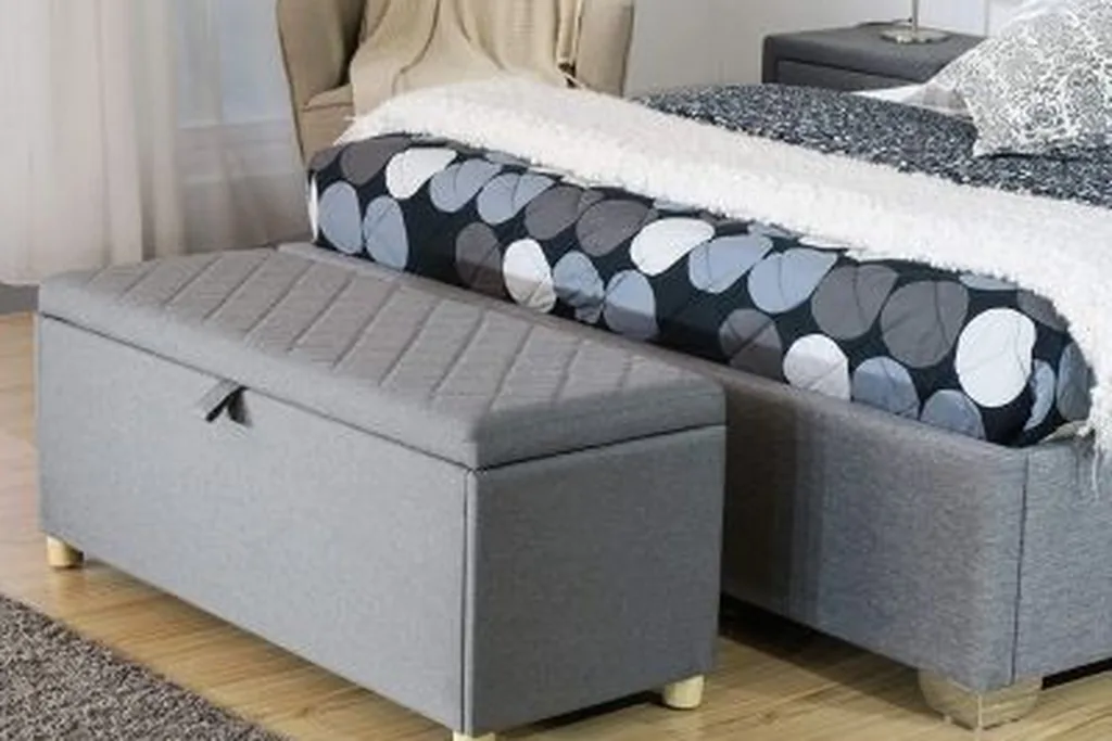 Storage ottoman beside a bedroom chair, open to show a folded throw.