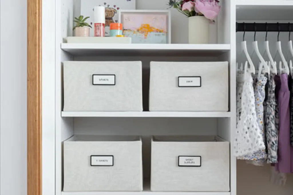 Labelled storage bins on a high closet shelf holding seasonal clothes.