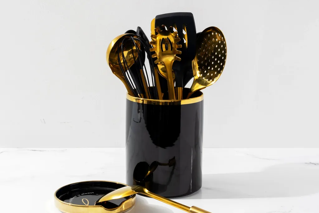 Gold cooking utensils in a black crock with a gold spoon rest on a white counter.