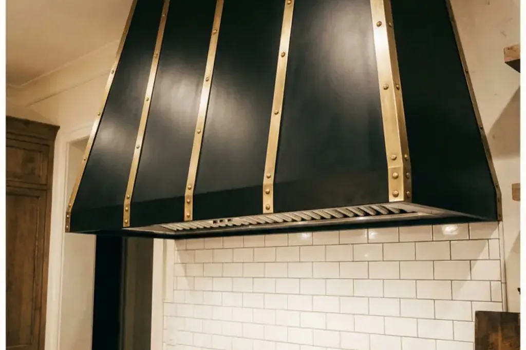 Black range hood with brass straps above a range and white subway tile.