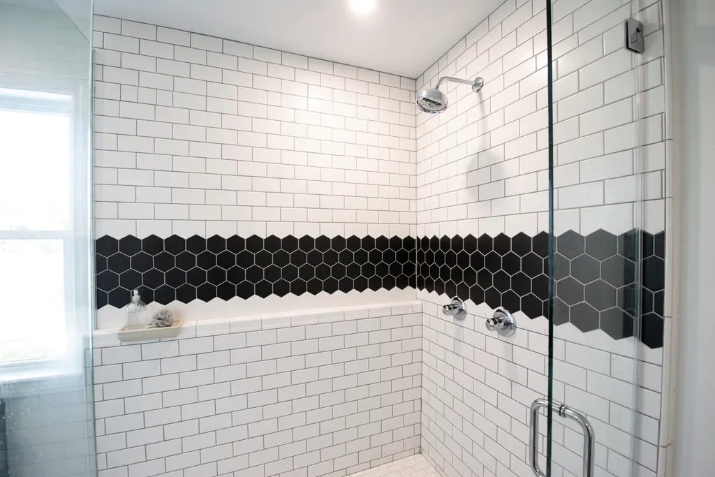 White shower wall with a horizontal band of black hexagon tiles at eye level.