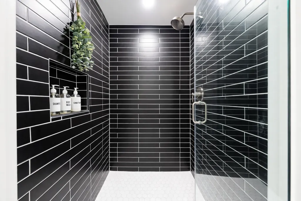 Shower tiled in black subway tiles with white grout lines and a white shower floor.