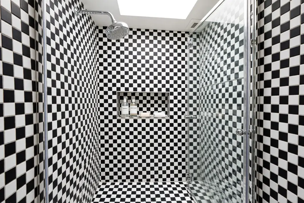 Small black and white checkerboard tiles on shower walls with a glass door.