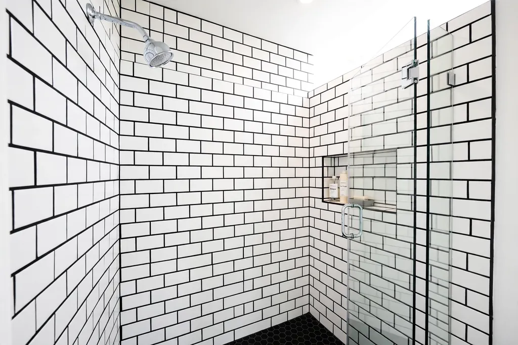 White subway tile shower wall with black grout lines and a chrome showerhead.