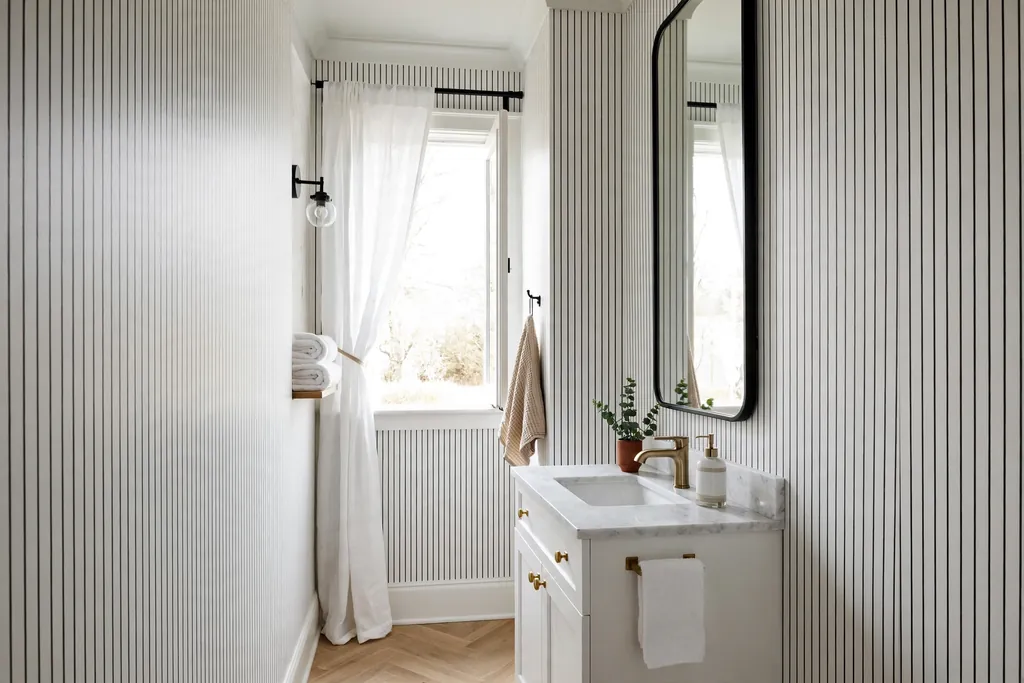 Narrow bathroom with fine black pinstripe wallpaper on white walls, white vanity, and tall mirror.