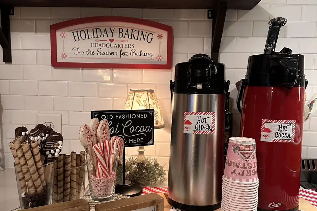 Hot cocoa station with drink dispensers, candy canes, and a holiday baking sign.