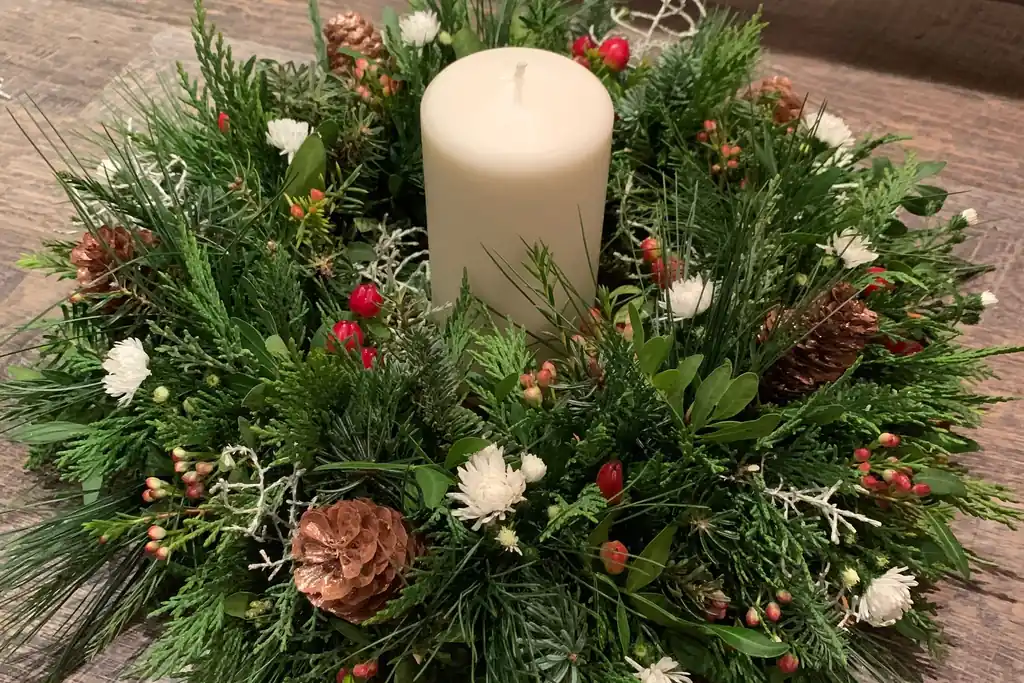 Evergreen wreath laid flat with a large cream pillar candle in the center.