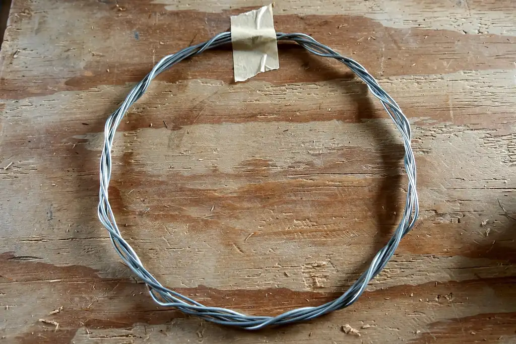 A bare wire wreath frame lying flat on a table, with a small tape mark at the top.
