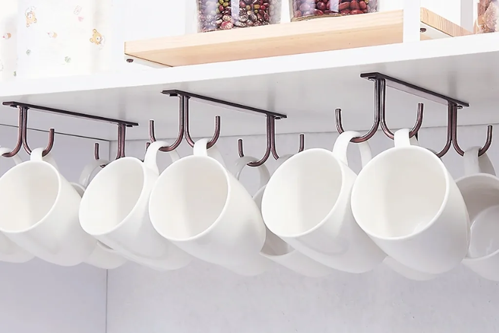 Coffee mugs hanging from hooks fitted under a kitchen cabinet.
