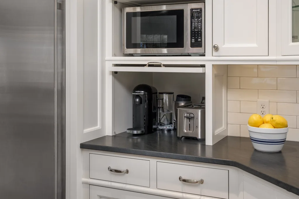 Counter cabinet with a lift up door raised over a coffee maker and toaster, microwave on the shelf above.