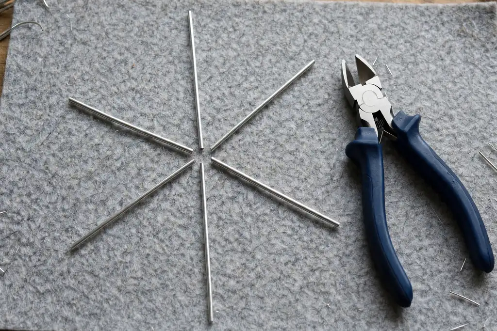 Six equal lengths of silver craft wire laid out in a star shape on a felt mat beside wire cutters.