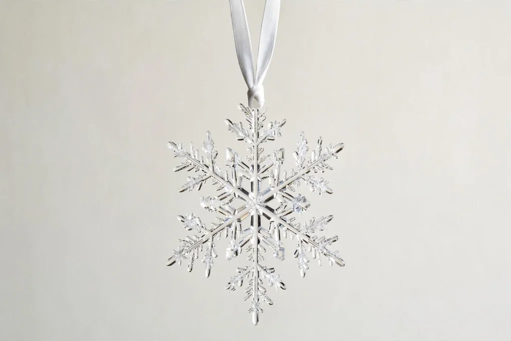 A crystal snowflake ornament with a white ribbon hanging loop tied at its top point, held up against a plain background.