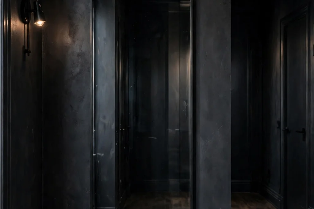 Dark hallway wall with an arched mirror in a thin black frame.