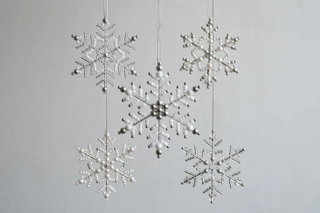 Beaded snowflake ornaments in white and silver hanging against a plain background.