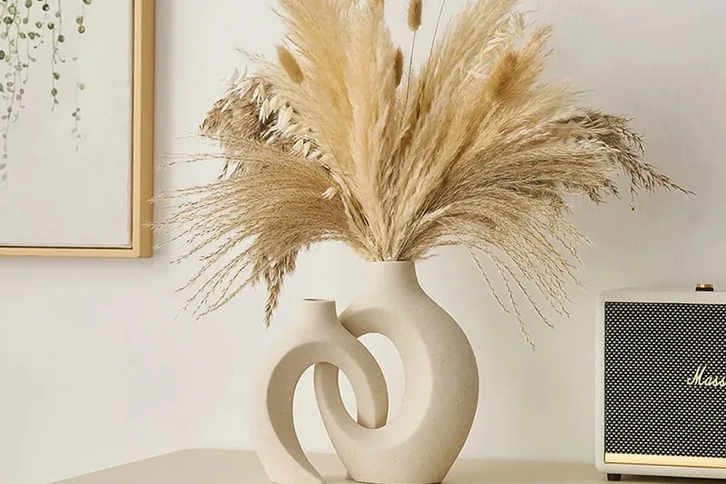 Dried pampas grasses in a white vase on a dresser.