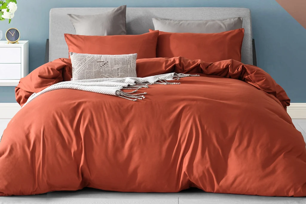 Bed made with a rust orange duvet cover set and matching pillows.