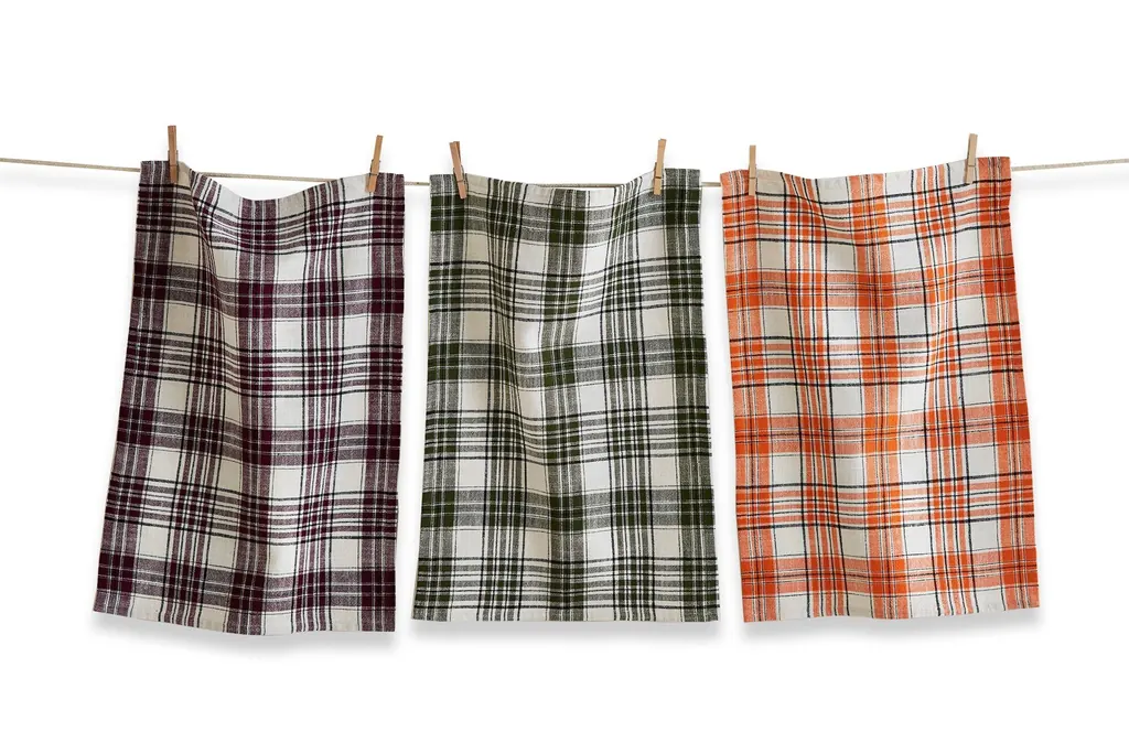 Plaid linen dish towels in warm fall colors hanging beside a kitchen counter.