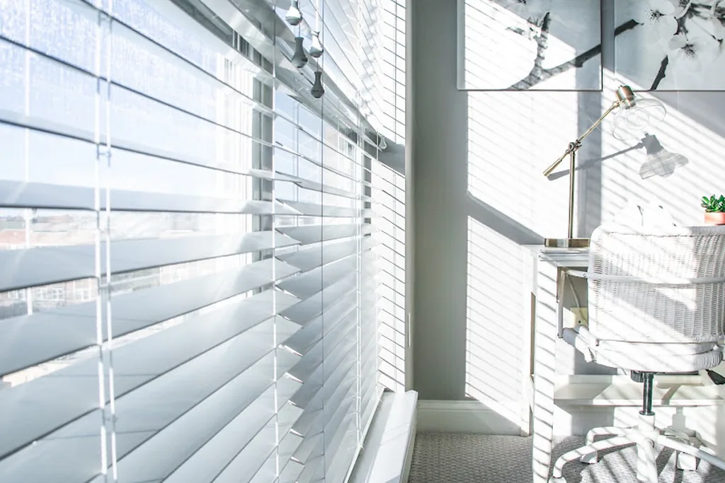 White blinds filtering bright sunlight at a studio window.