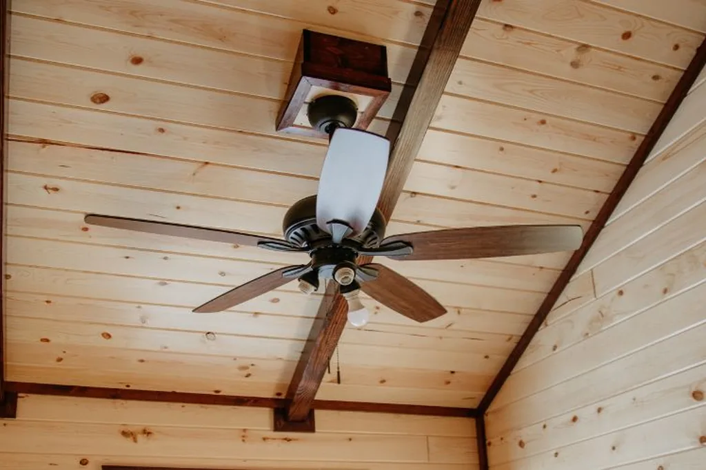 Ceiling fan fitted to the wood panelled ceiling of a small studio.