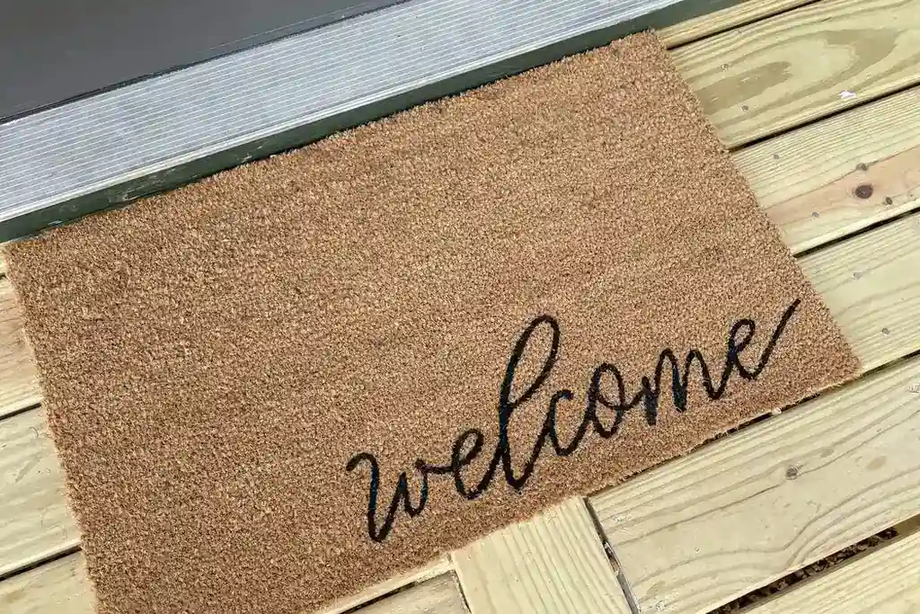 Welcome mat on a wood deck outside a studio door.