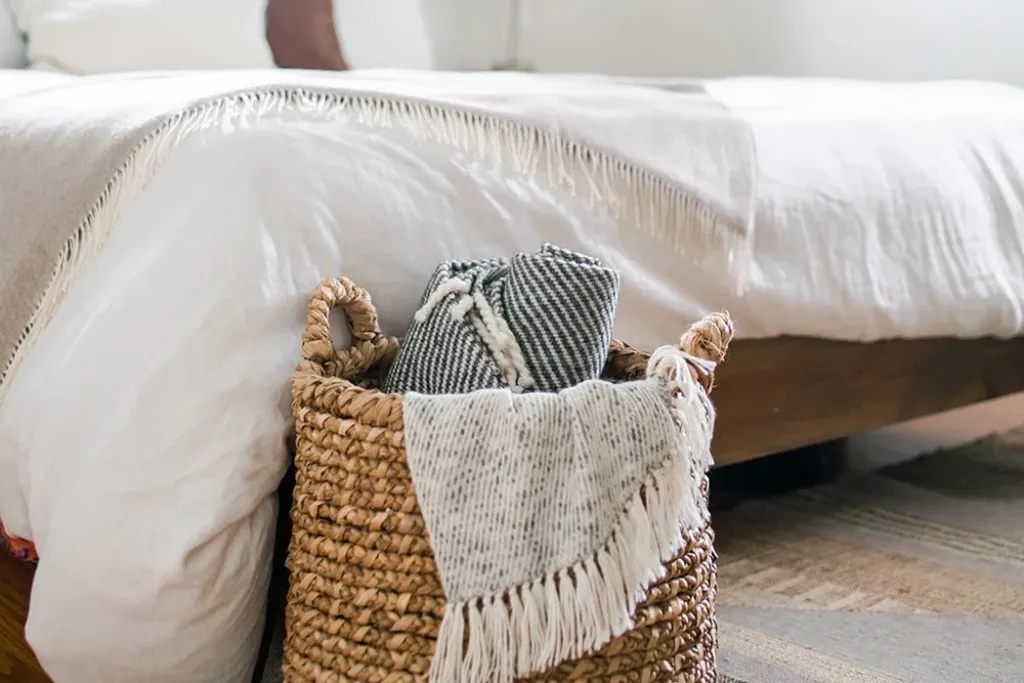 Basket with a folded throw at the foot of a bed.