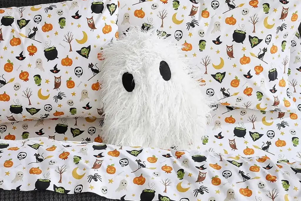 Small ghost shaped pillow on a bed with plain pillows.