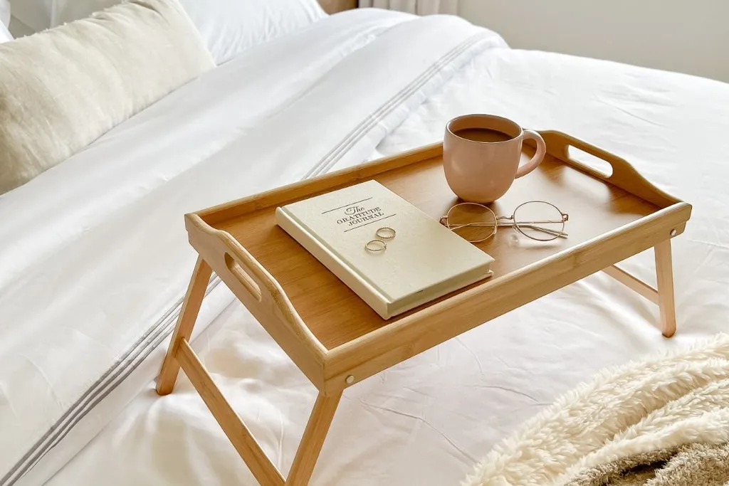 Tray with a book and mug on a chair beside a bed.