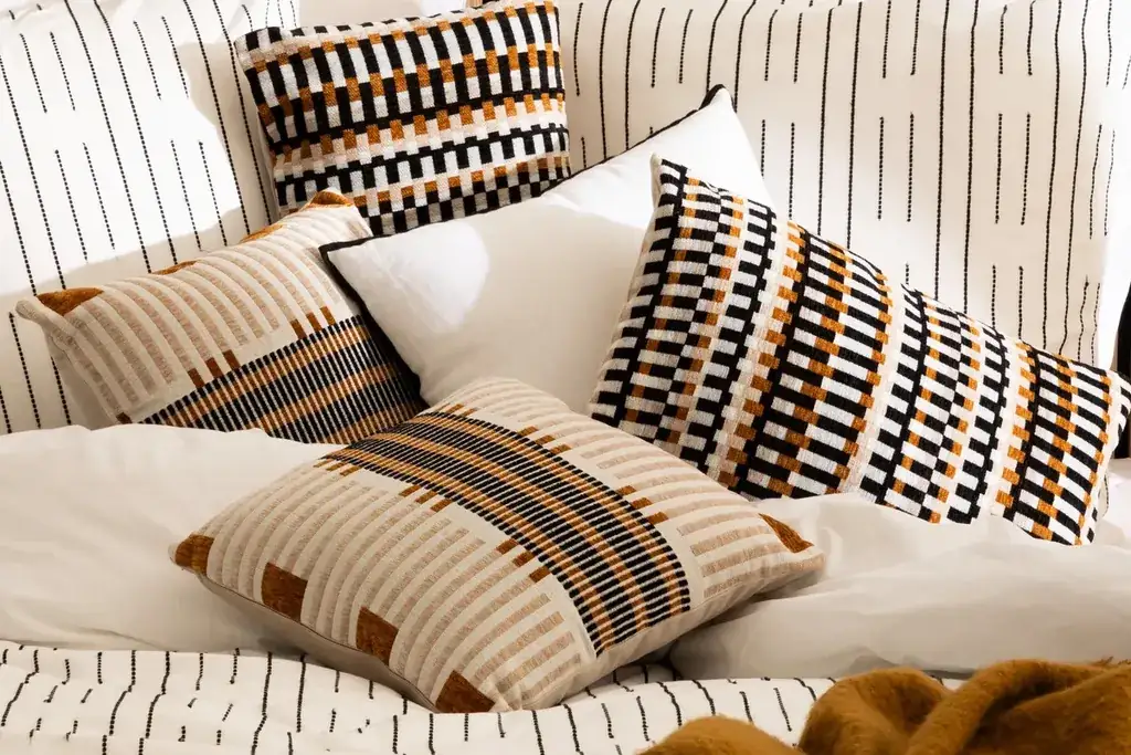 Textured pillows in black, cream, and rust on a bed.