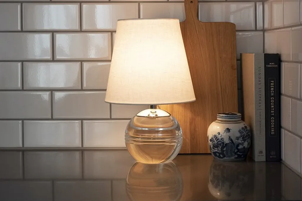 Small lamp with a cream shade glowing on a kitchen counter.