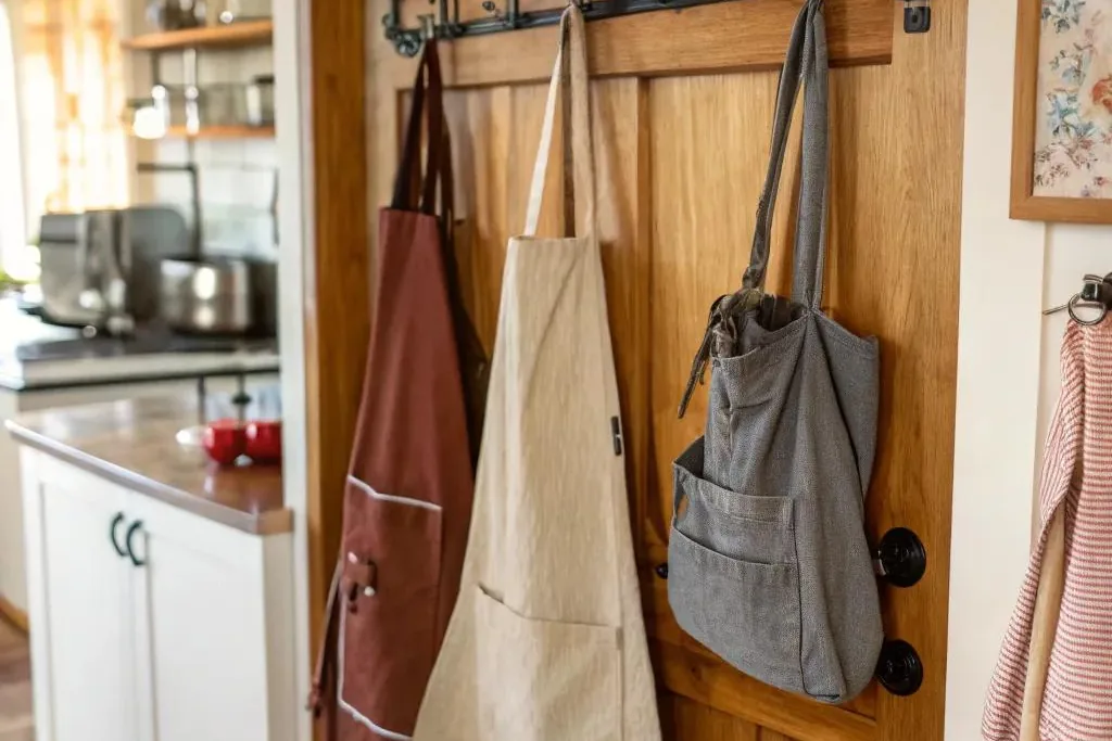 Aprons and tote bags hanging on hooks by a wooden kitchen door.