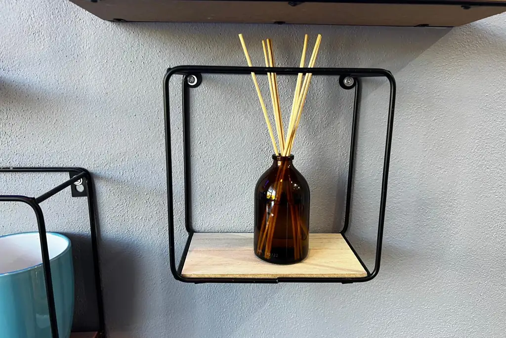 Amber reed diffuser bottle on a small wall mounted shelf.