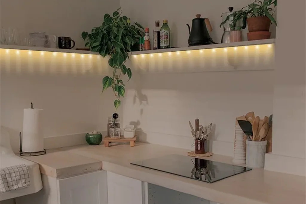 Warm LED light strip glowing under a kitchen shelf above a counter.