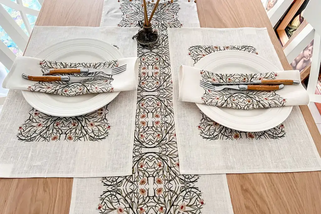 Dining table with a patterned runner and placemats set with plates and napkins.