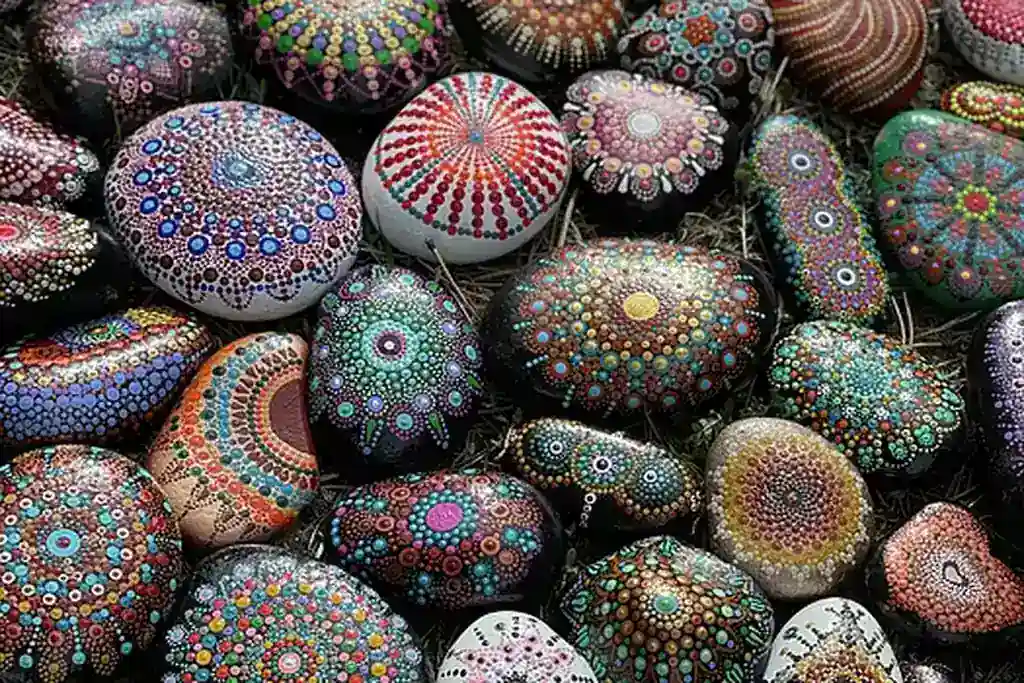 Flat stones painted with simple colorful patterns set among plants.