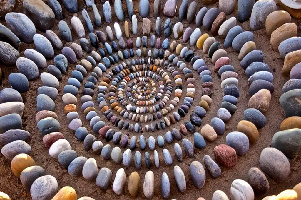 Circular pebble mandala laid out on the ground in a garden.