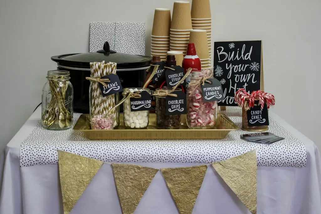 Dining table with a central tray of cocoa jars, paper cups, and a build your own sign.