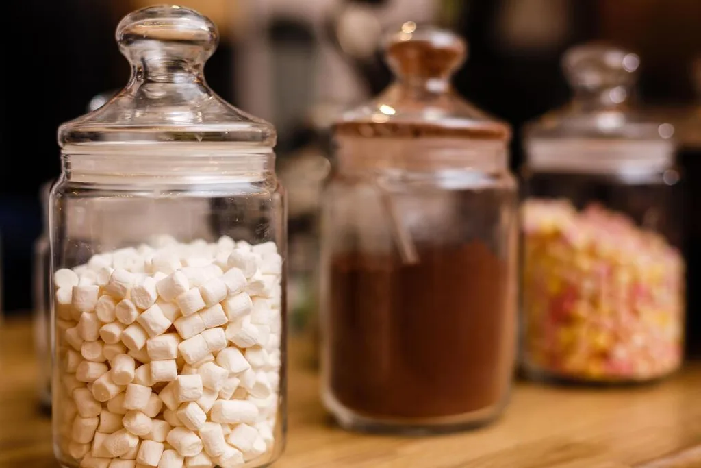 Glass jars filled with marshmallows and cocoa powder on a wooden counter.