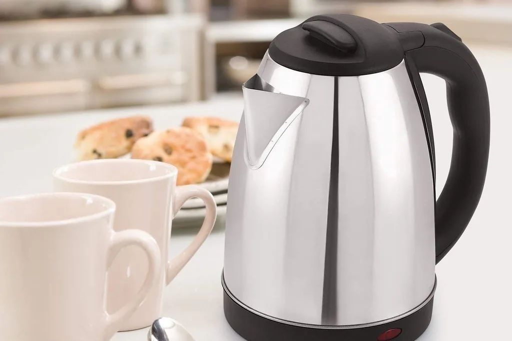 Stainless electric kettle on a counter with two white mugs.