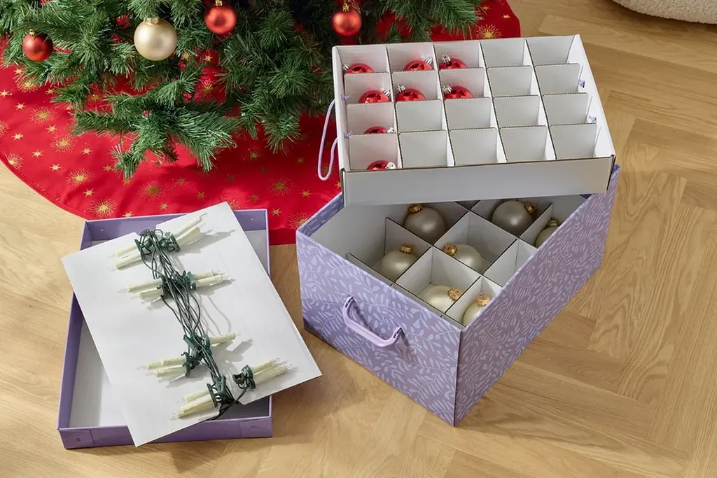 Divided storage box being packed with seasonal items beside a Christmas tree.