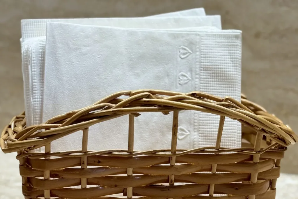 Wicker basket holding folded white napkins and linens.