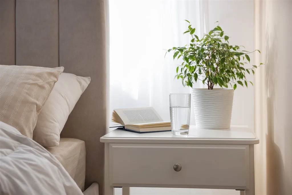 Bedside tray holding a book, water glass, and glasses on a clear nightstand