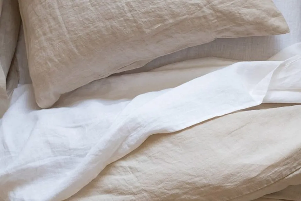 Layers of cotton and linen bedding folded back on a bed