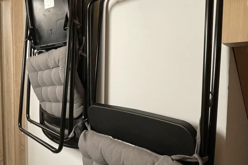 Folding chairs hanging flat on hooks on a balcony wall.