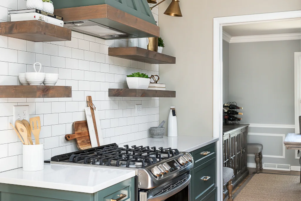 Deep green painted range hood and green cabinets over a stove with white tile walls.