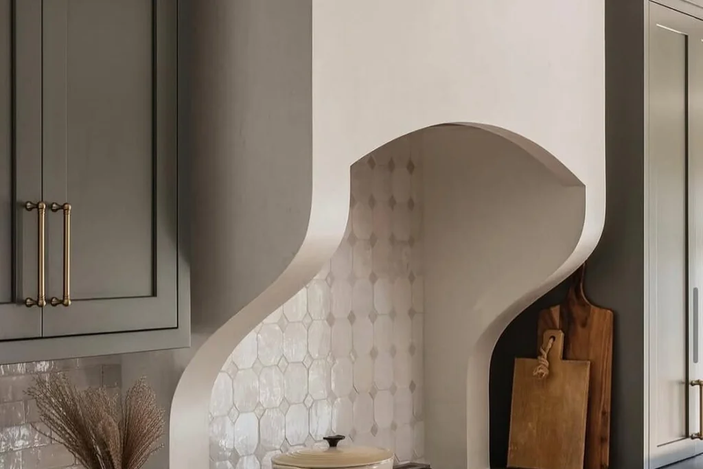 Plaster range hood with a soft curved apron above a tiled kitchen wall.