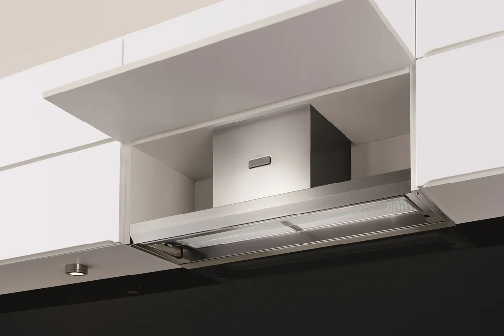 Slim slide out range hood fitted under white wall cabinets in a small kitchen.