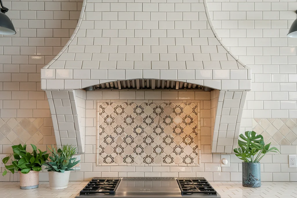 Range hood clad in white subway tiles over a stove with a patterned tile backsplash.