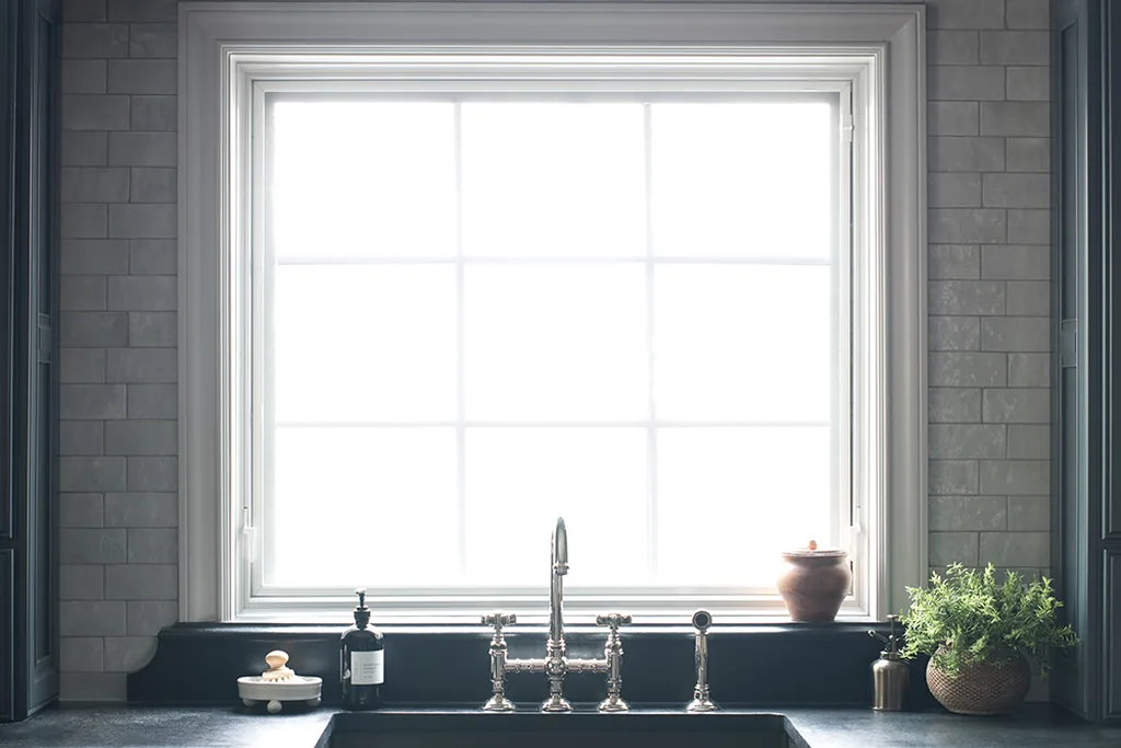 Uncovered kitchen window with a deep sill holding a small plant and a soap dish above a dark sink.